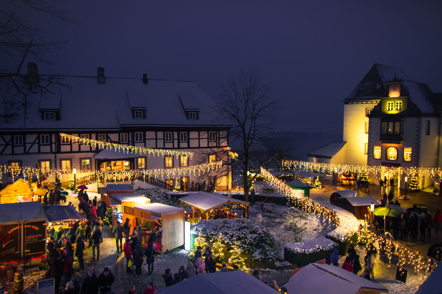 Blick auf den Schlosshof beim Weihnachtsmarkt, schneebedeckte Hütten, Lichterketten